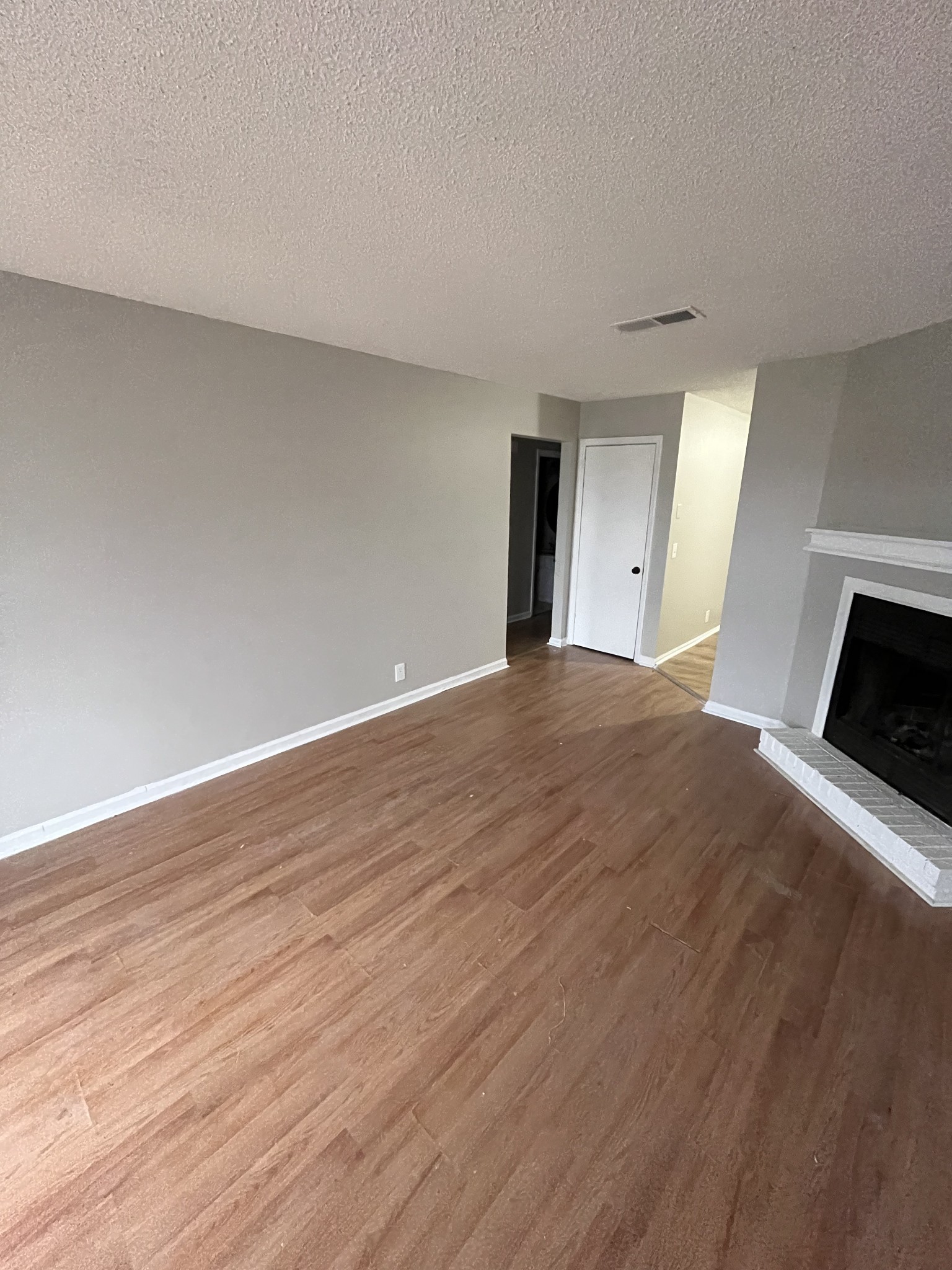 a view of an empty room with wooden floor fireplace and a window