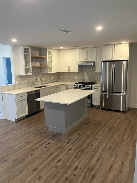 a large kitchen with stainless steel appliances granite countertop a stove a sink dishwasher a refrigerator and white cabinets with wooden floor