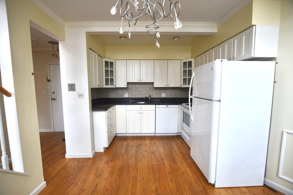 a kitchen with granite countertop a refrigerator a sink and white cabinets