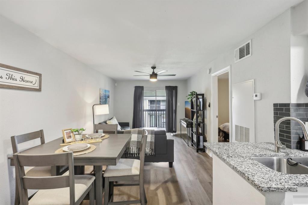 This is a modern, open-concept living space featuring a neat dining area adjacent to a well-appointed kitchen with granite countertops. The area is well-lit with natural light from the balcony doors and includes contemporary furnishings.