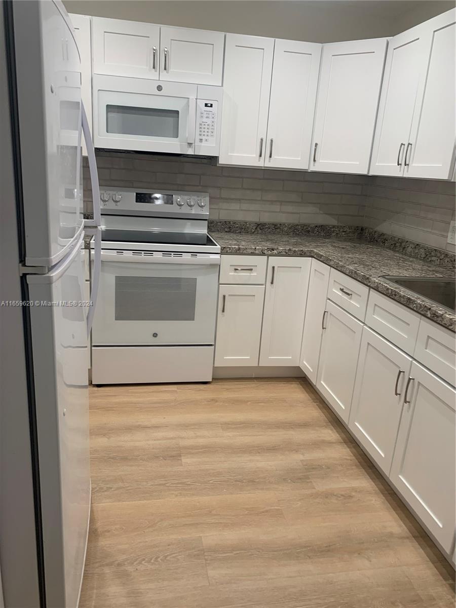 a kitchen with granite countertop white cabinets and white appliances