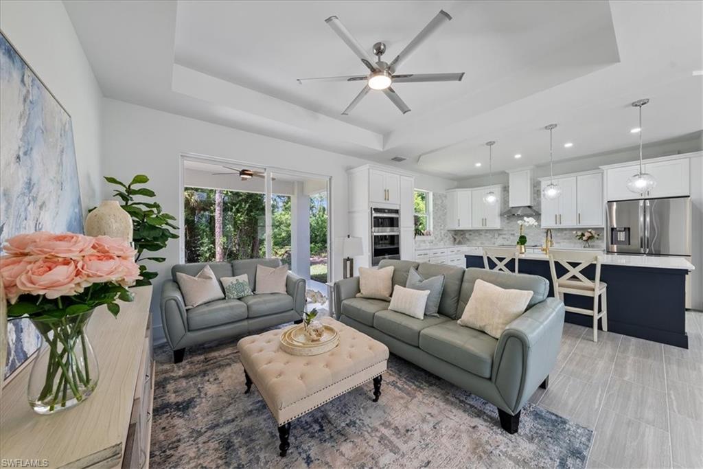 Living room with light tile patterned flooring, ceiling fan, and a tray ceiling