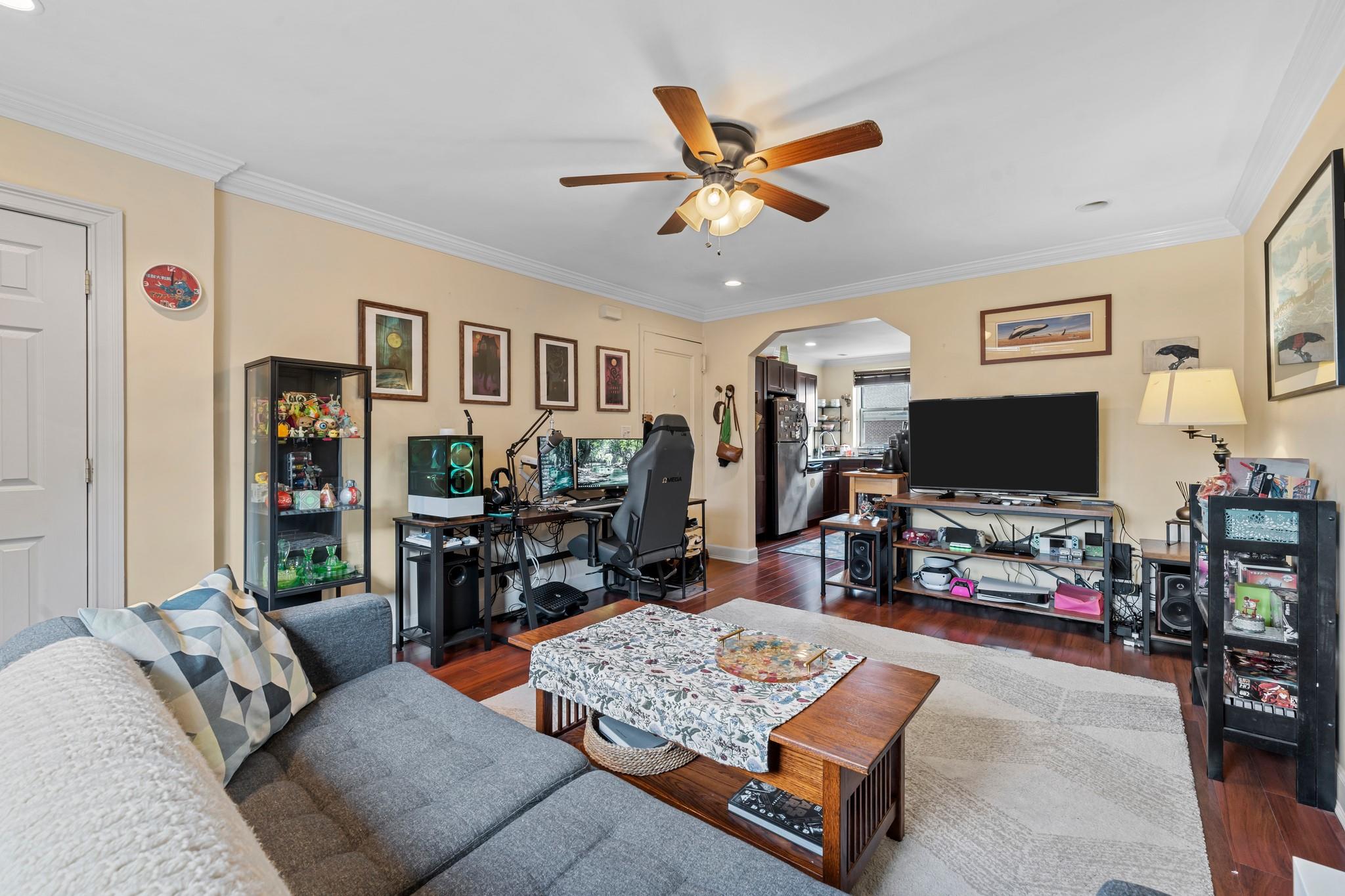 Living room featuring ceiling fan, dark wood-type flooring, and ornamental molding