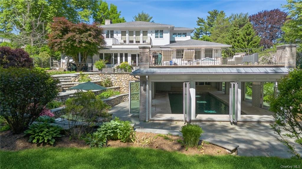 Rear view of property with multiple tired patios, stone walls, specimen plantings and irrigated gardens.