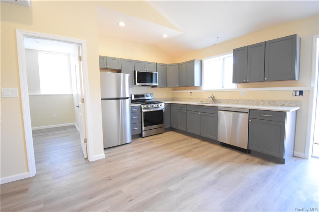 Kitchen featuring light hardwood / wood-style flooring, sink, vaulted ceiling, gray cabinets, and appliances with stainless steel finishes