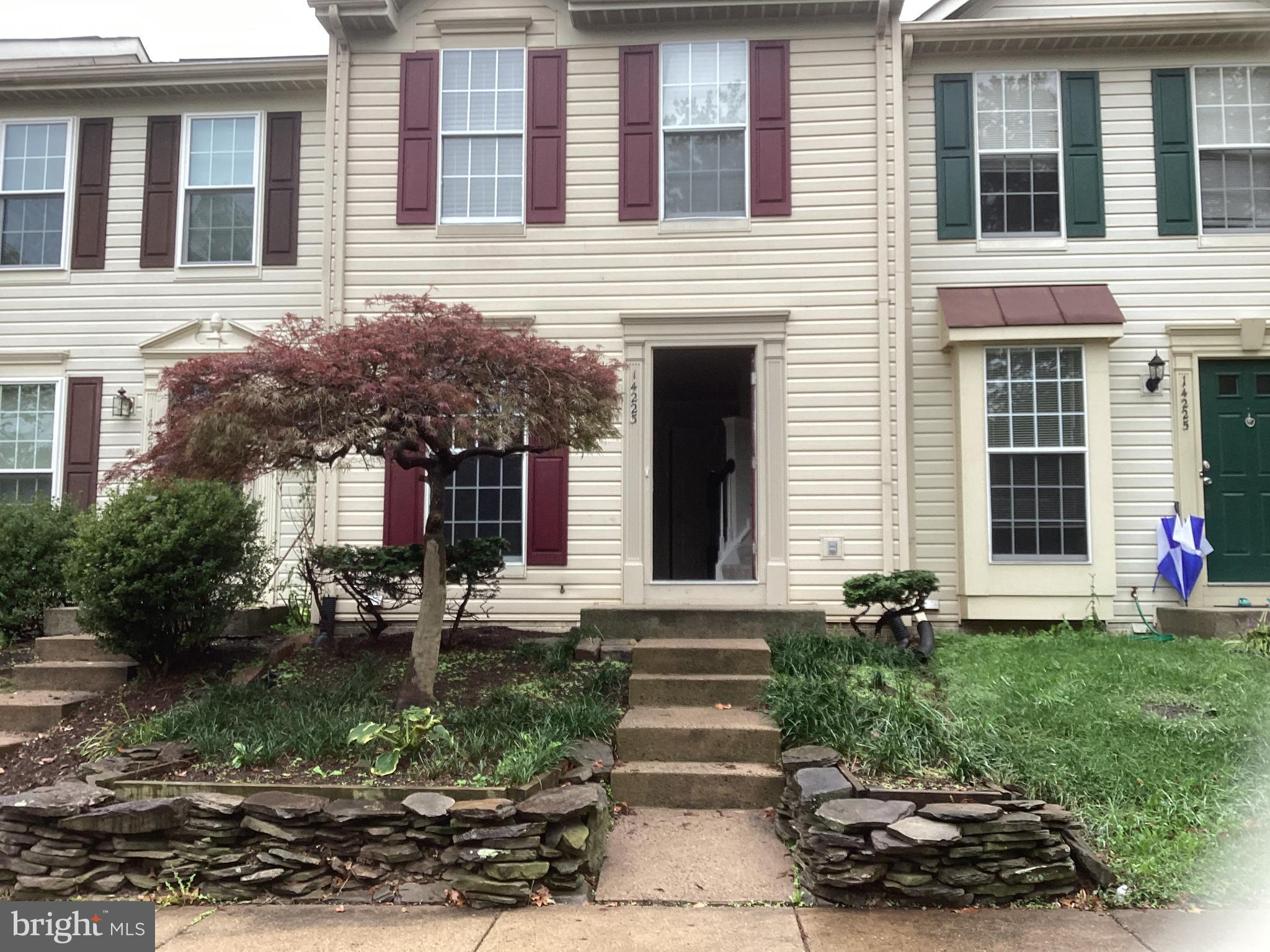 a view of a brick house with a yard plants and large tree