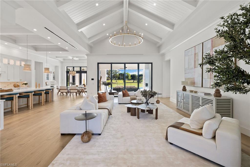 Living room with beamed ceiling, high vaulted ceiling, light wood-type flooring, and an inviting chandelier