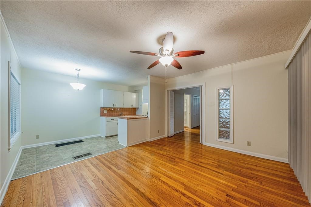 a view of an empty room with wooden floor and a kitchen