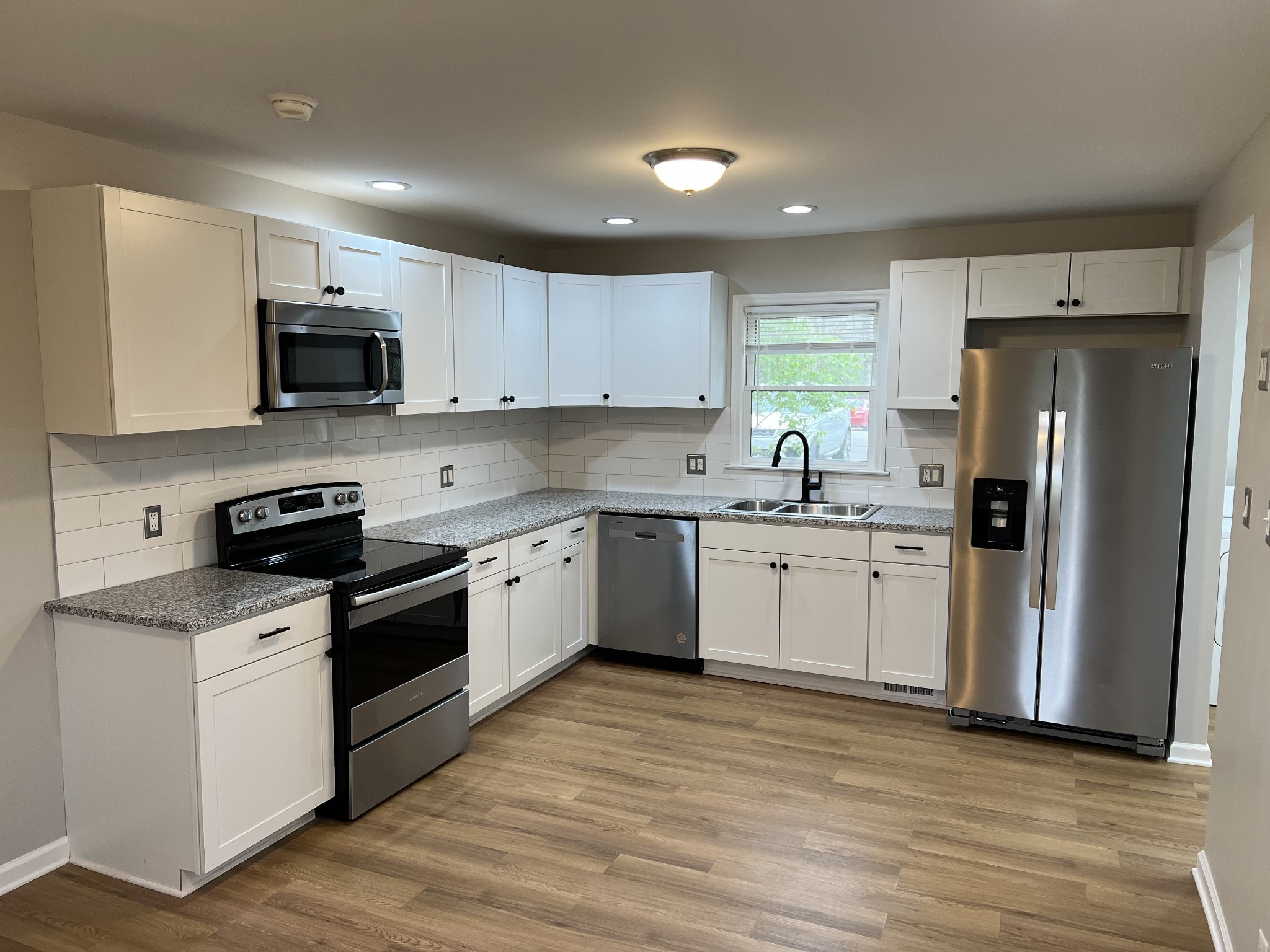 a kitchen with stainless steel appliances white cabinets a sink a stove a refrigerator and microwave