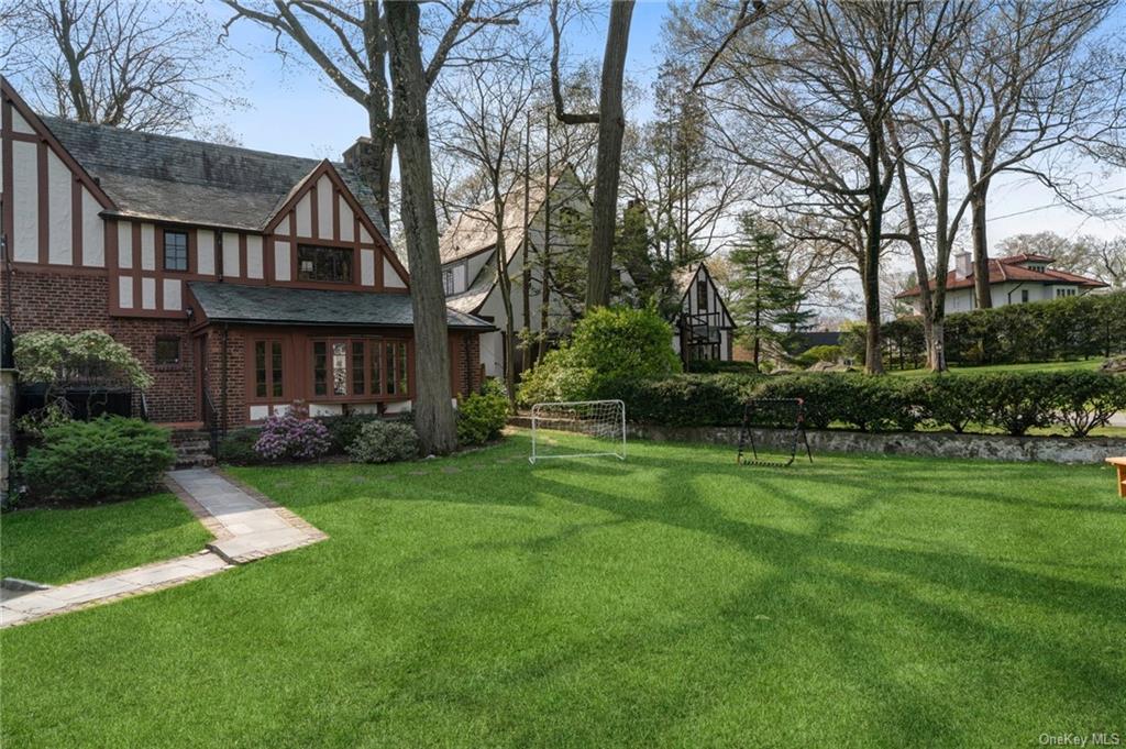 a view of a big yard in front of a brick house with plants and large trees