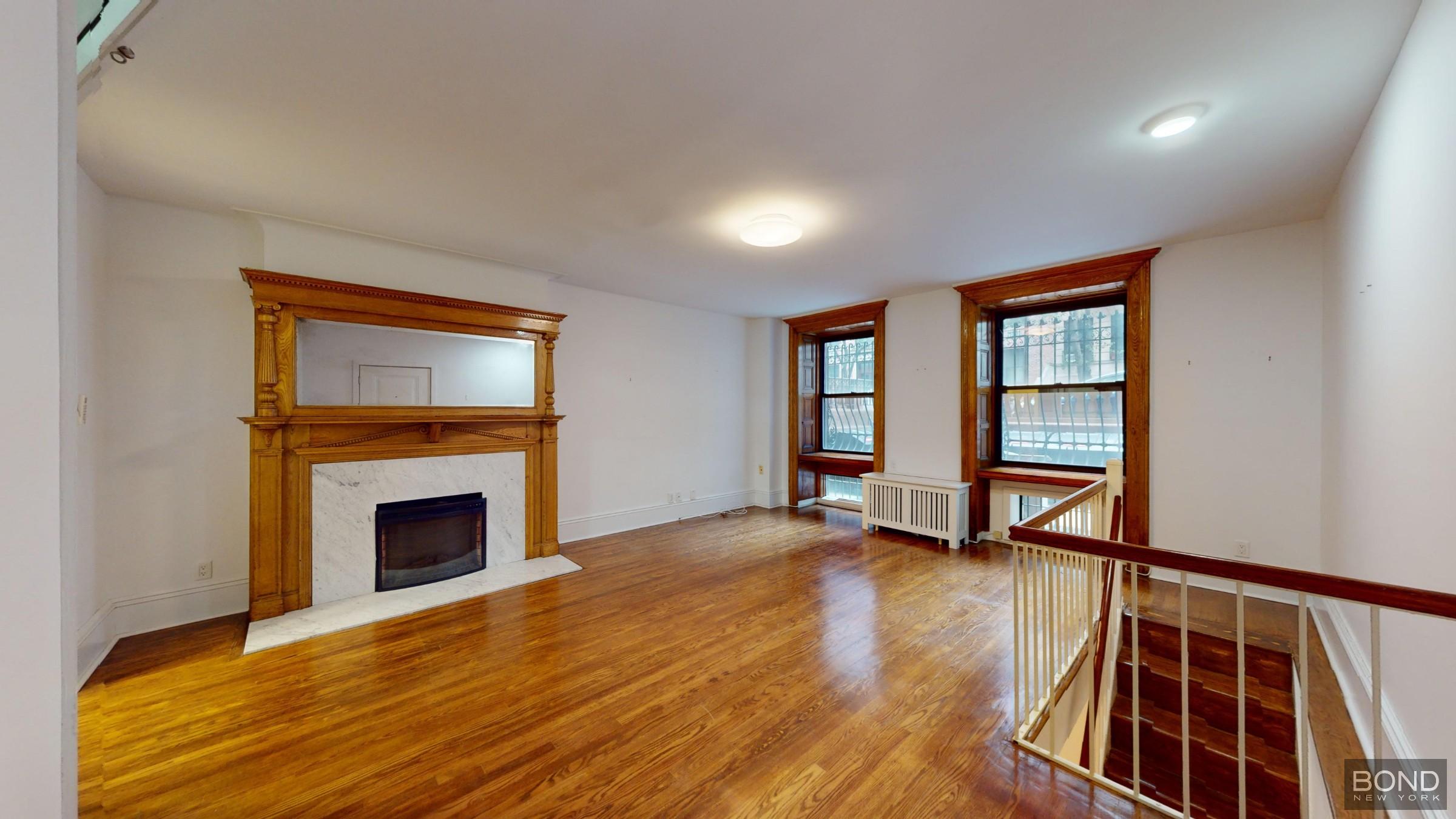 a view of an empty room with wooden floor fireplace and a window