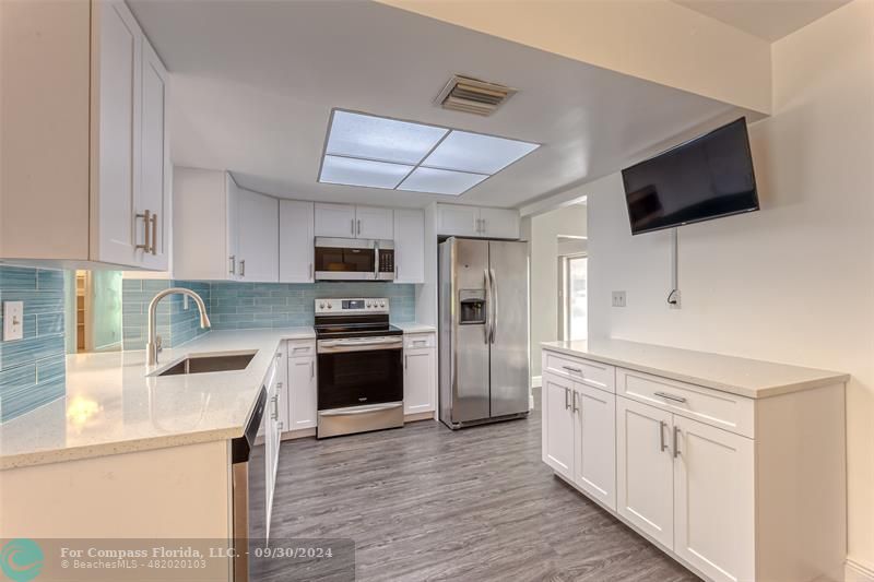 a kitchen with stainless steel appliances white cabinets a sink a stove a microwave and wooden floors