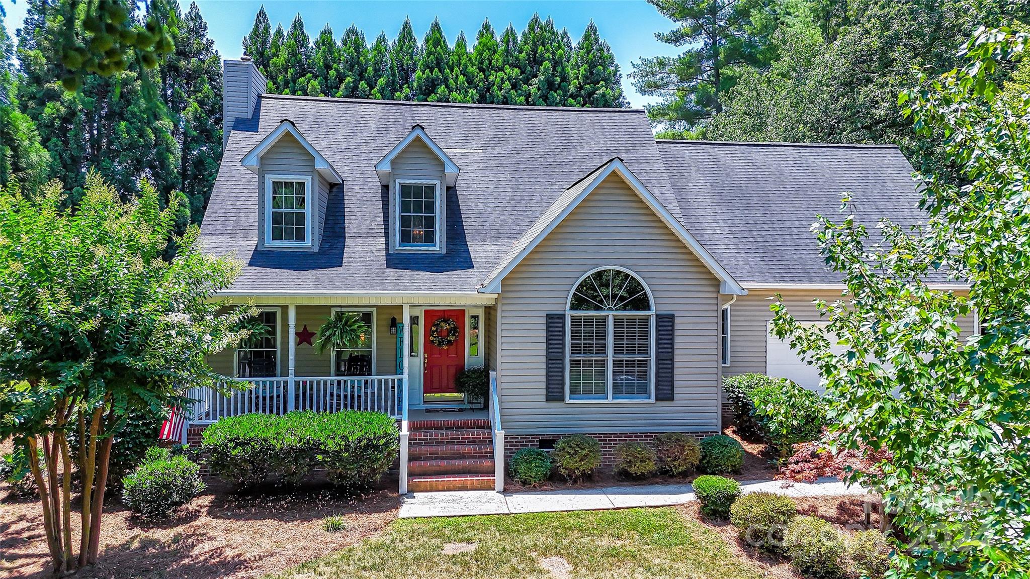 a view of a brick house with a yard plants and large tree