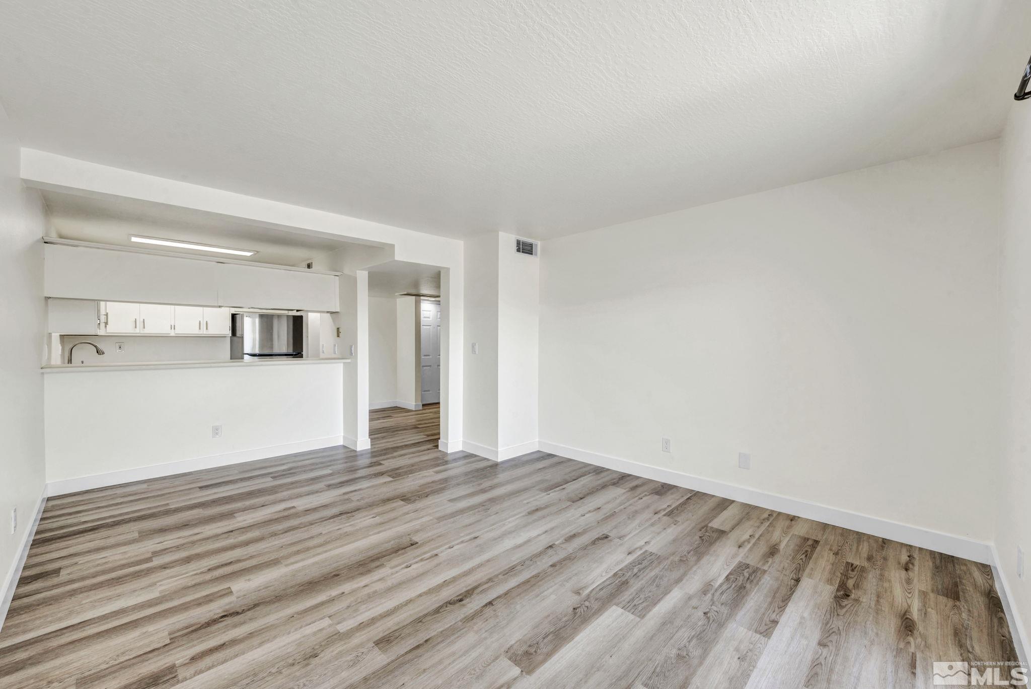 a view of empty room with wooden floor and kitchen view