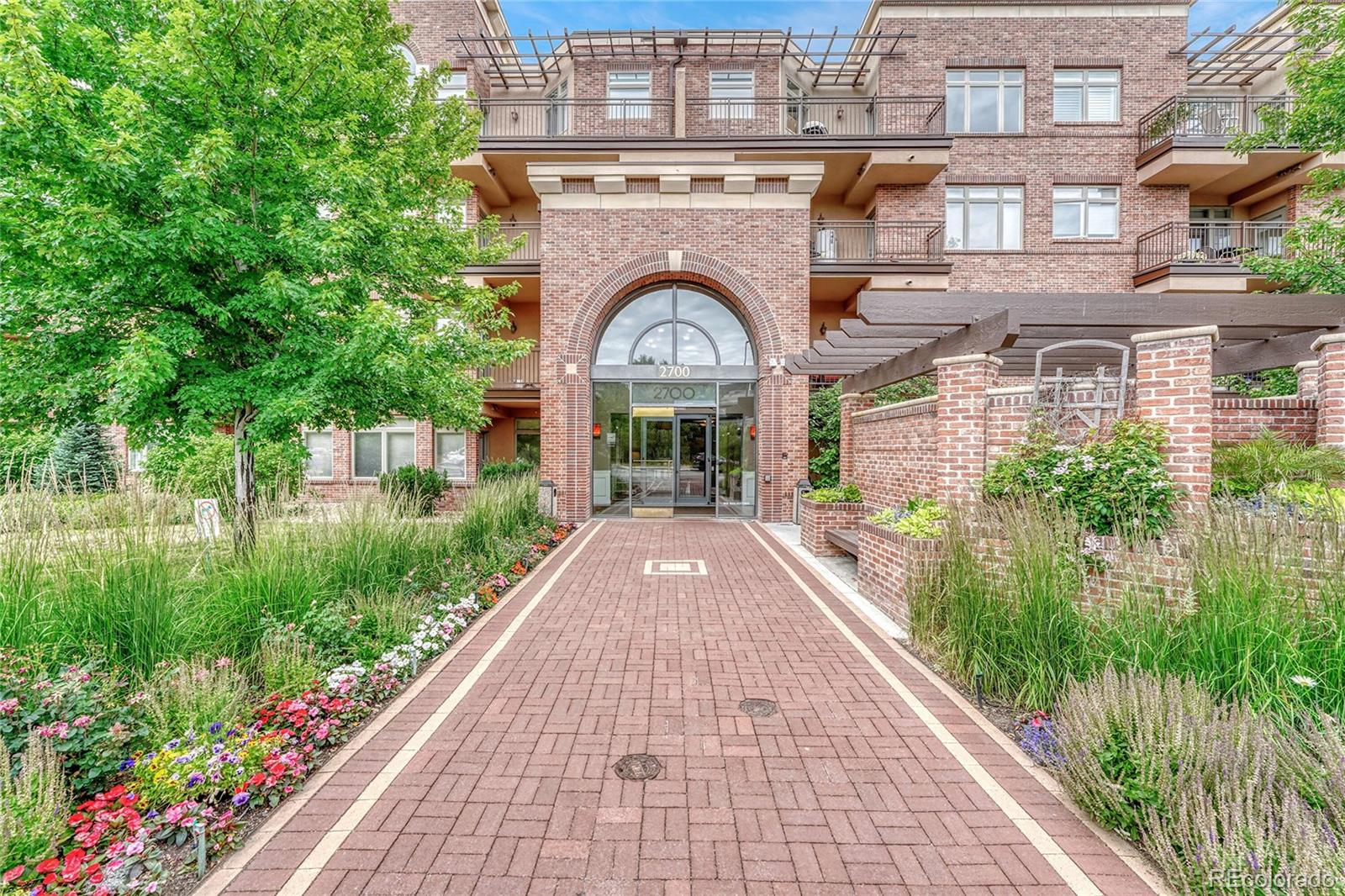 a view of a brick house with a small yard plants and a large tree