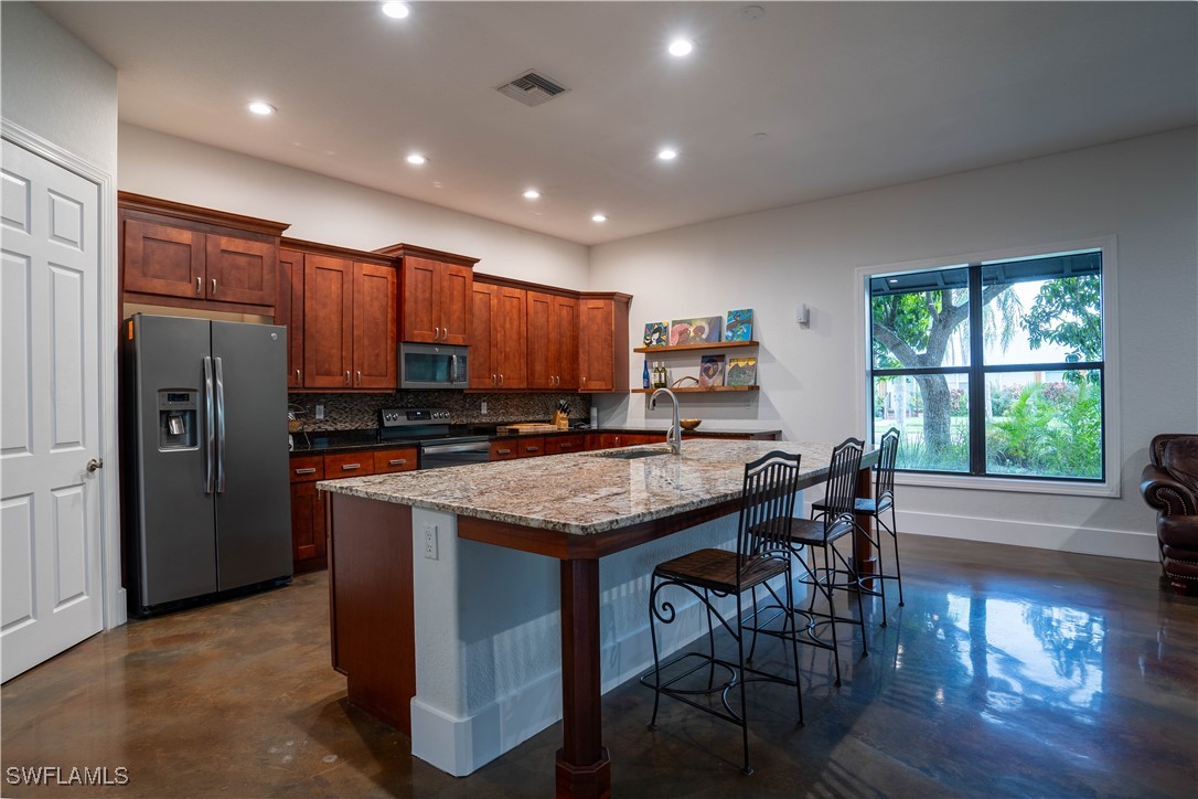 a kitchen with stainless steel appliances granite countertop a stove a refrigerator a kitchen island a table and chairs