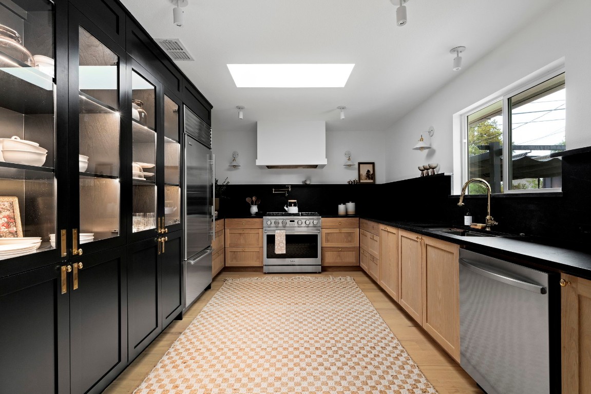 At the heart of the home is the stunning kitchen, complete with custom white oak cabinetry accented by Rejuvenation solid brass hardware. The space also boasts a 36" counter-depth Sub-Zero refrigerator, black mist granite countertops and backsplash, and an integrated LED-lit pantry with glass doors.