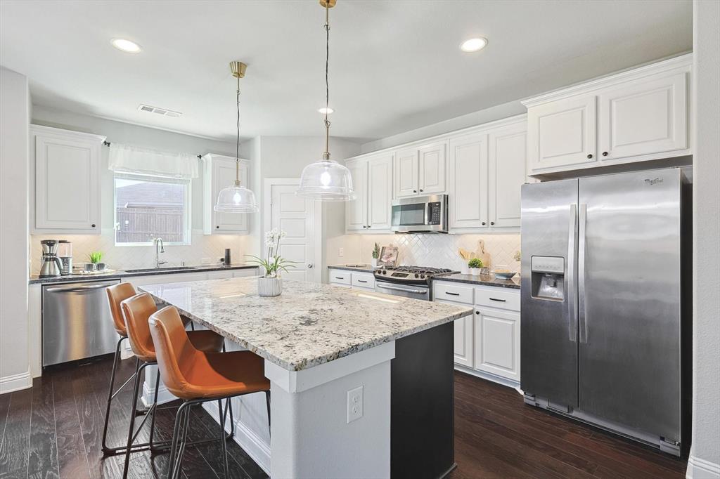 a kitchen with stainless steel appliances granite countertop a table chairs stove a sink dishwasher a refrigerator and microwave with wooden floor