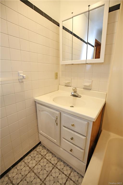 Bathroom with decorative backsplash, tile patterned floors, vanity, and tile walls