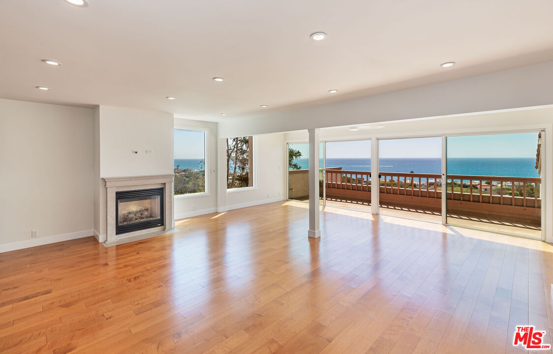 an empty room with wooden floor fireplace and windows