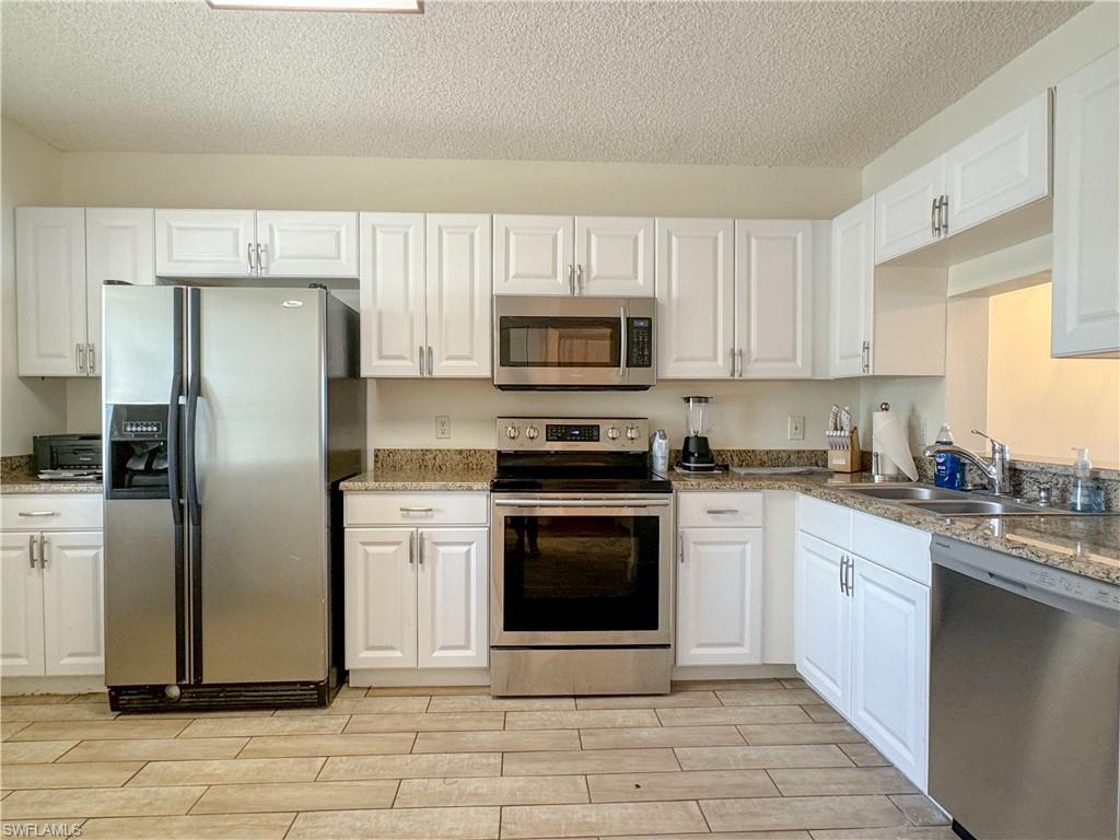 Kitchen with sink, a textured ceiling, light hardwood / wood-style flooring, white cabinetry, and stainless steel appliances