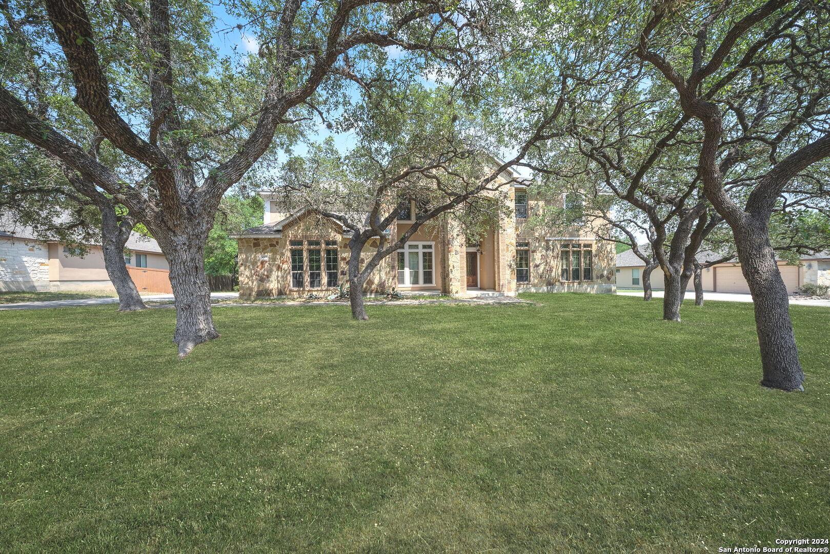 a view of white house in front of a big yard with large trees