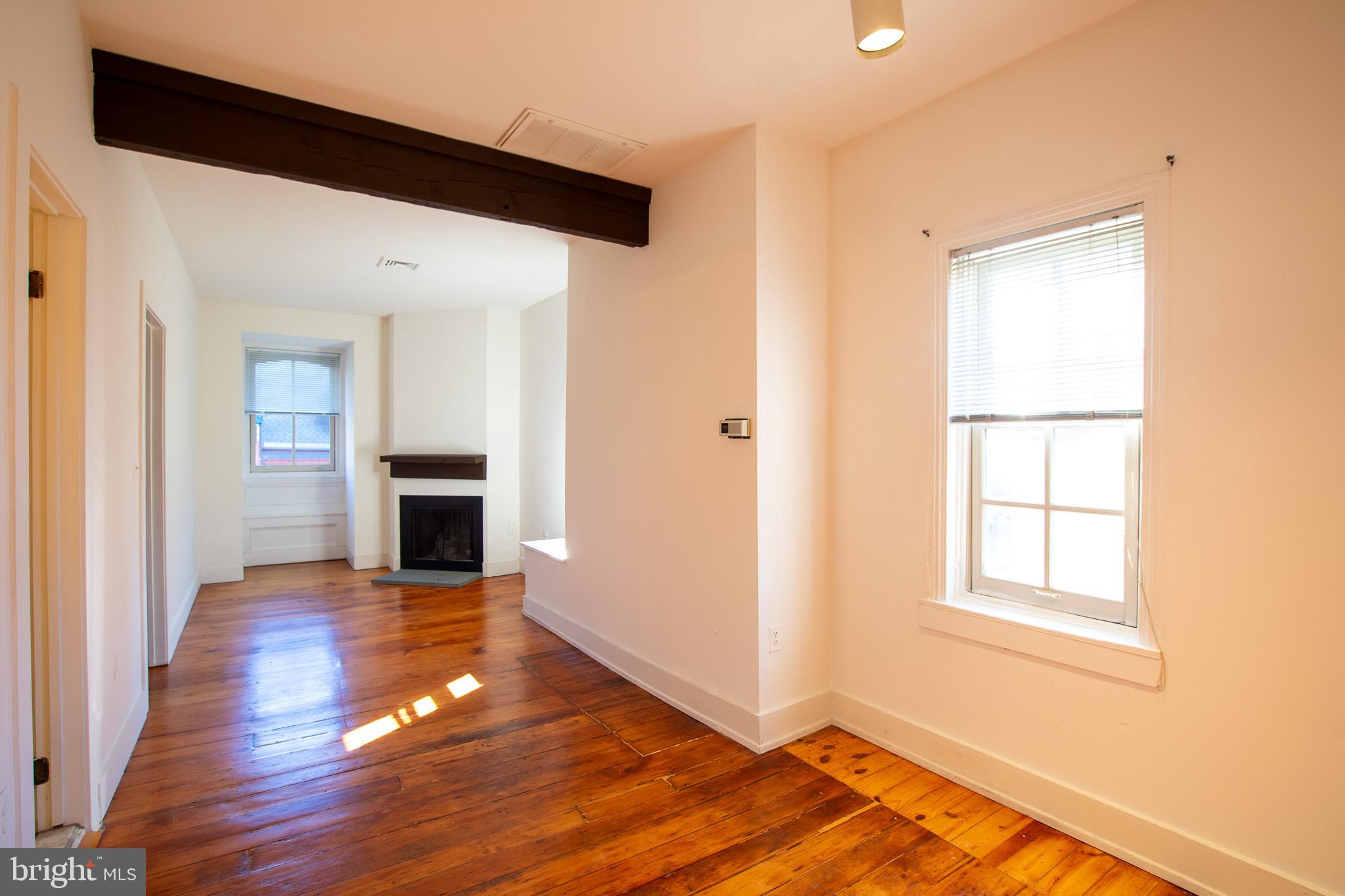 an empty room with wooden floor fireplace and windows