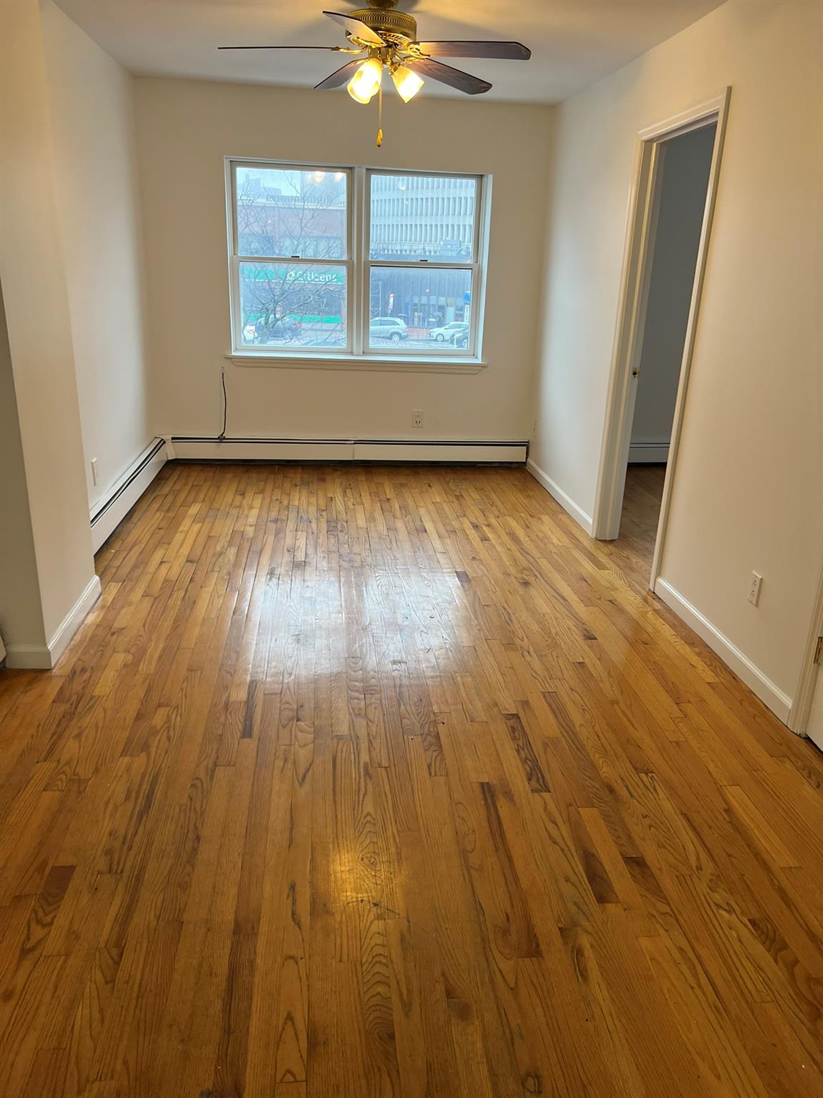 an empty room with wooden floor fan and window