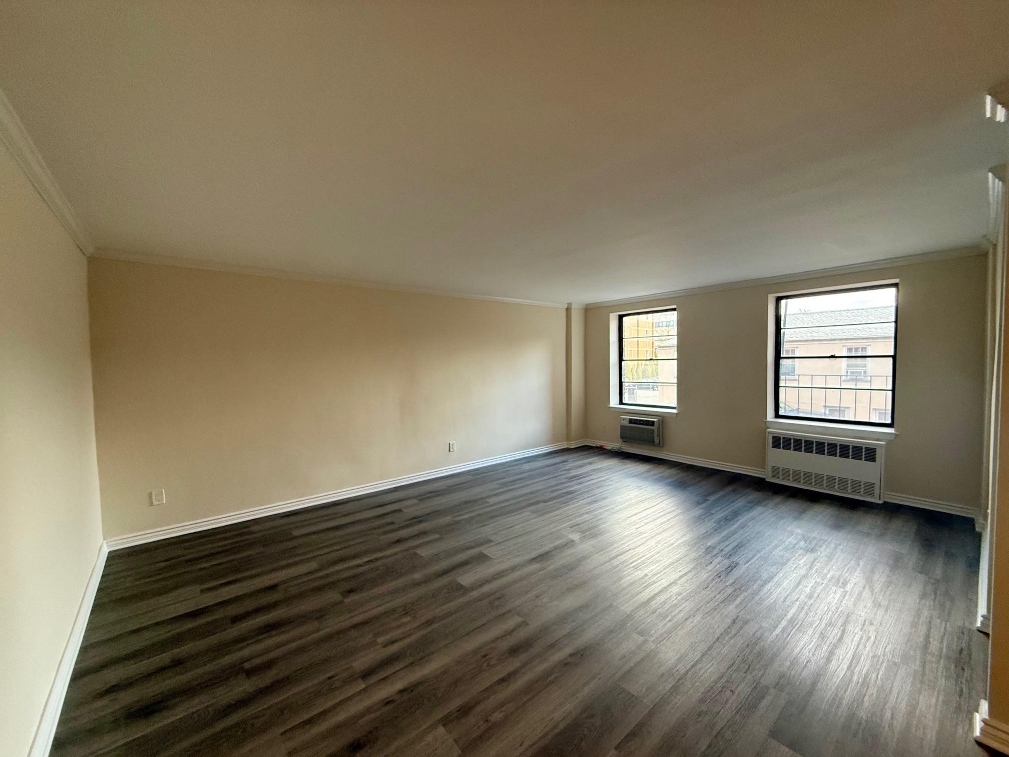 a view of an empty room with wooden floor and window