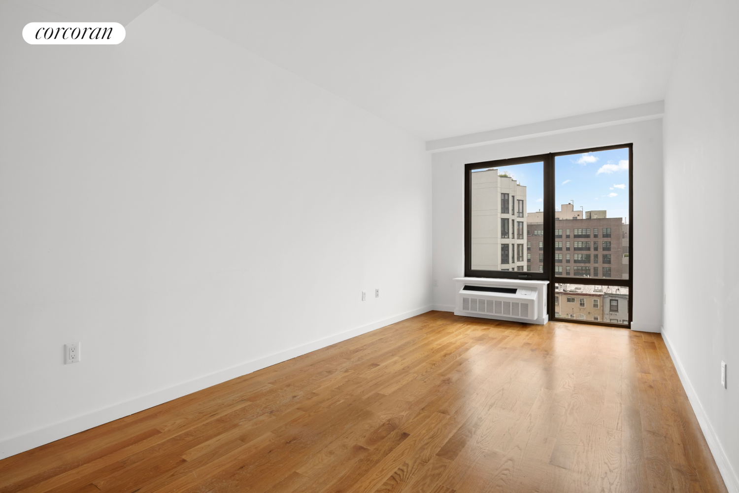 a view of an empty room with wooden floor and a window