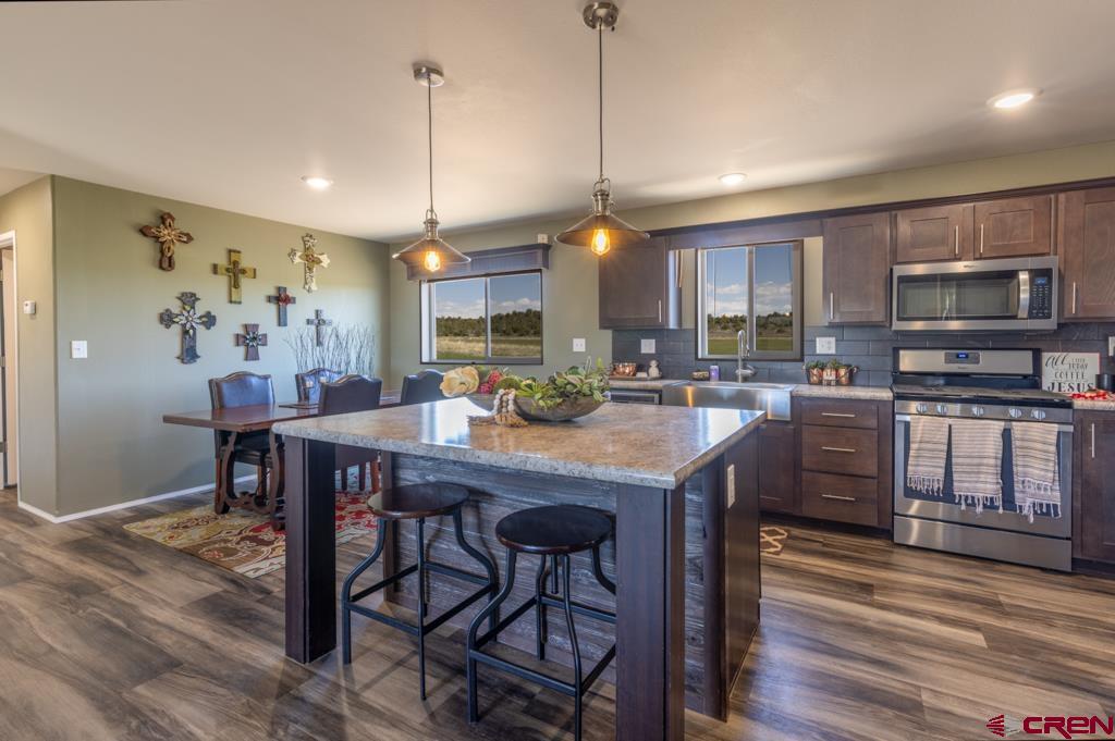 a kitchen with stainless steel appliances granite countertop a stove a refrigerator a kitchen island a dining table and chairs with wooden floor