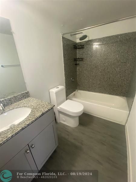 a bathroom with a granite countertop sink a toilet a mirror and bathtub