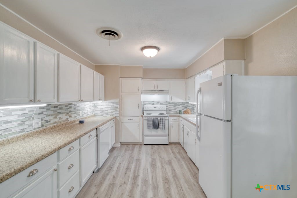 a kitchen with granite countertop a refrigerator sink and white cabinets