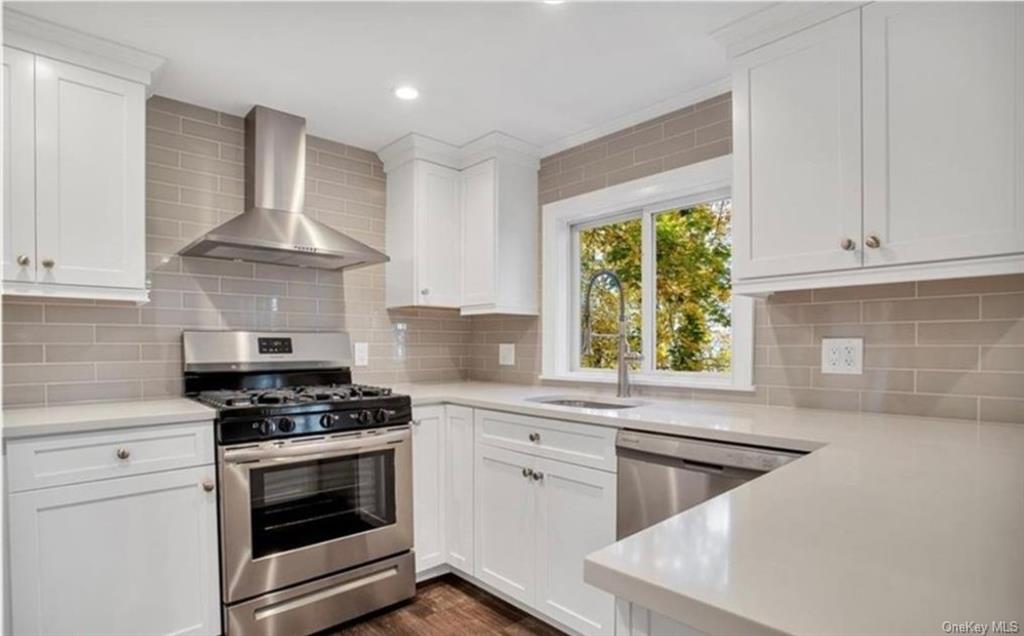 Kitchen featuring white cabinetry, wall chimney range hood, and appliances with stainless steel finishes