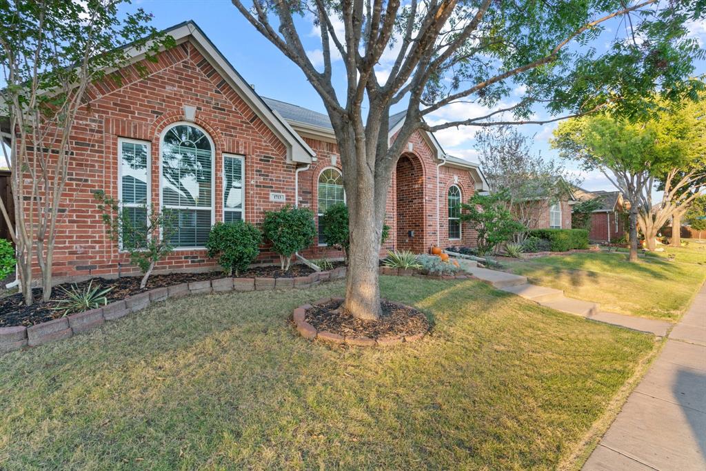 a view of a house with brick walls plants and large tree