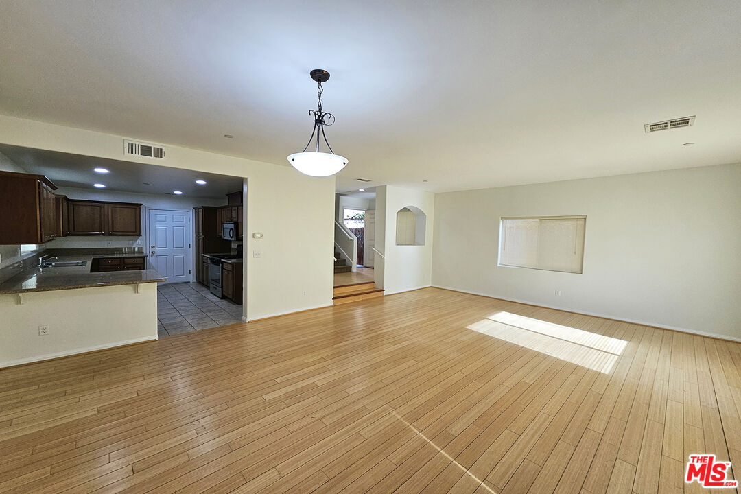 a view of an empty room with wooden floor and a kitchen