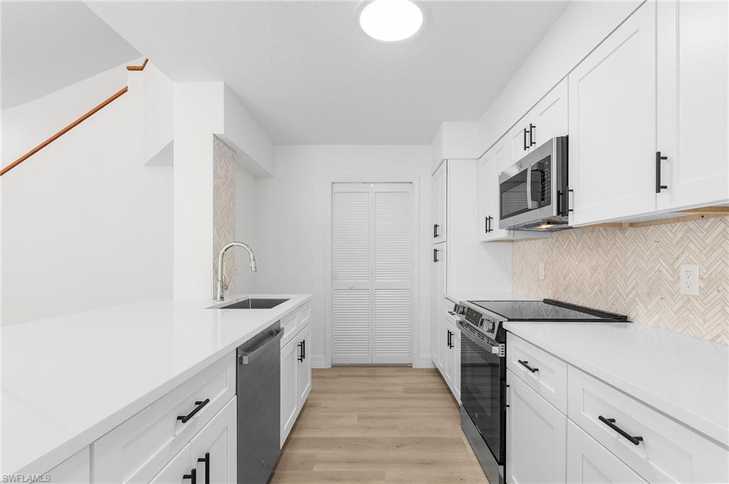 Kitchen with decorative backsplash, light wood-type flooring, stainless steel appliances, sink, and white cabinetry