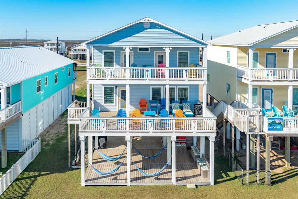 2930 Bluewater, a charming beach house features a two-story design with multiple decks, colorful outdoor seating, and hammocks underneath. It offers a relaxed coastal vibe, perfect for enjoying seaside living.