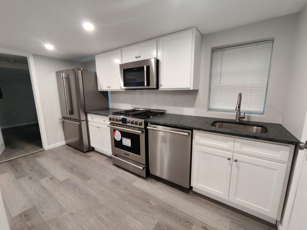 Kitchen with dark stone counters, white cabinets, sink, light wood-type flooring, and stainless steel appliances