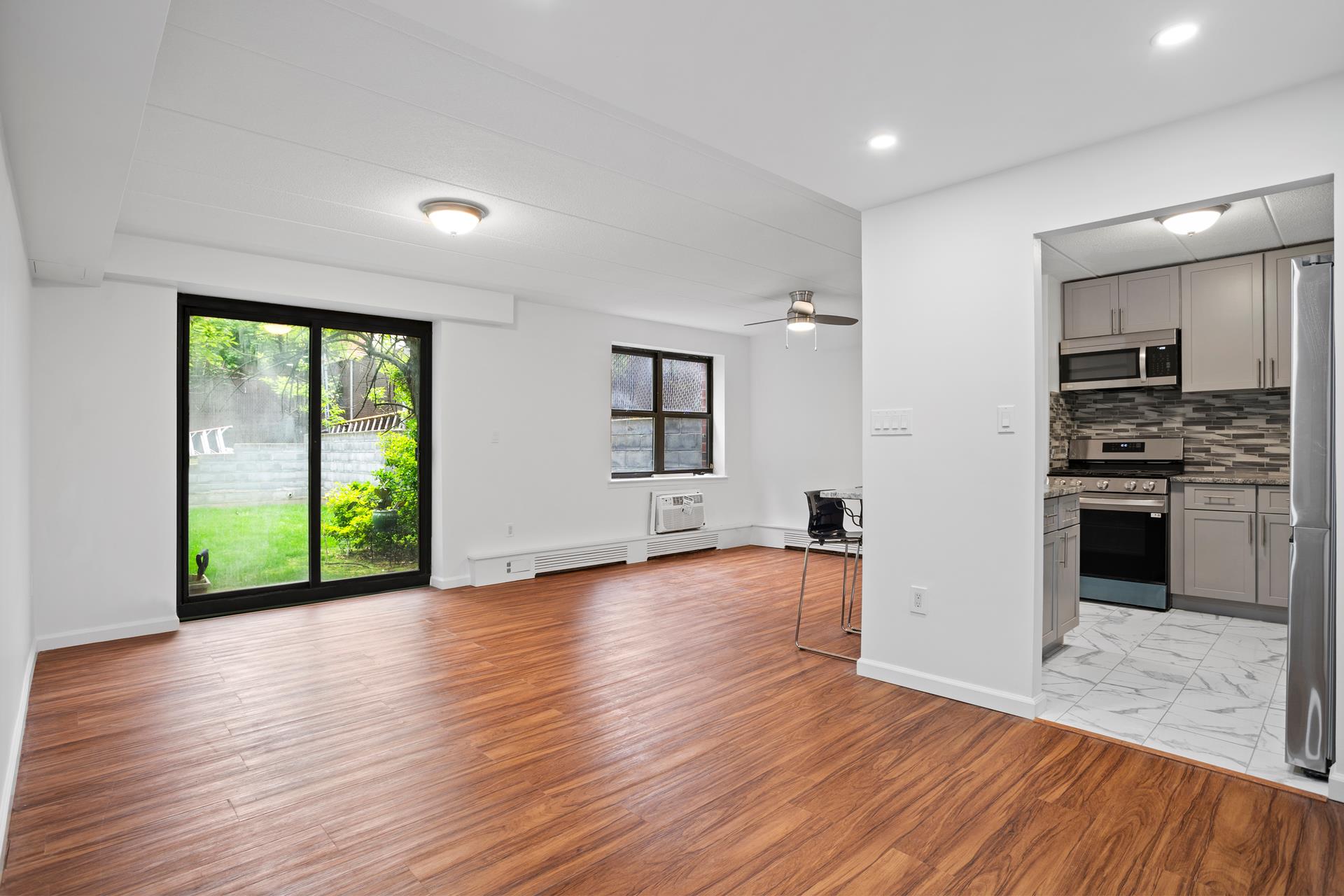 an empty room with wooden floor kitchen view and windows