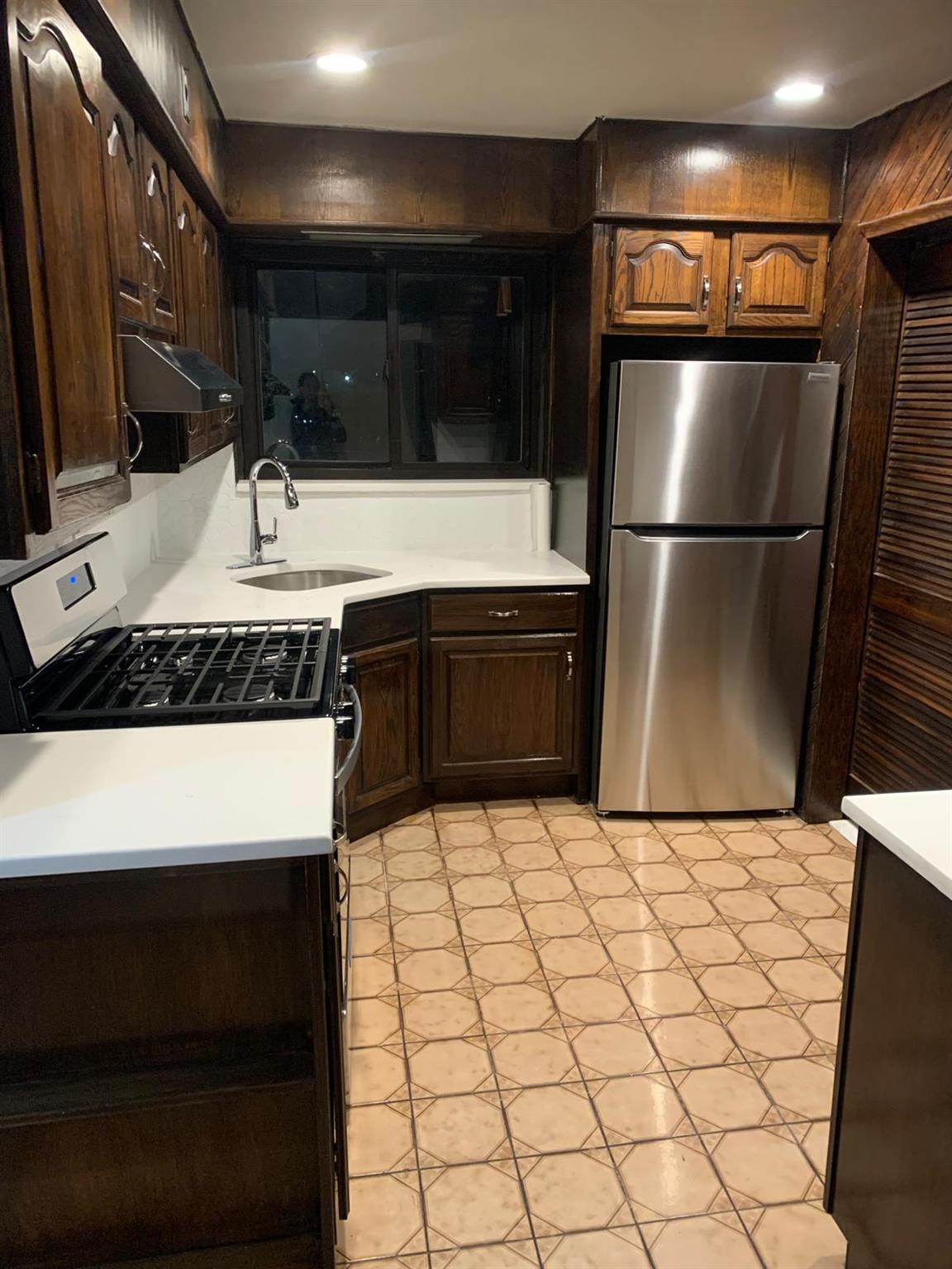 Kitchen with exhaust hood, sink, stainless steel fridge, dark brown cabinets, and range