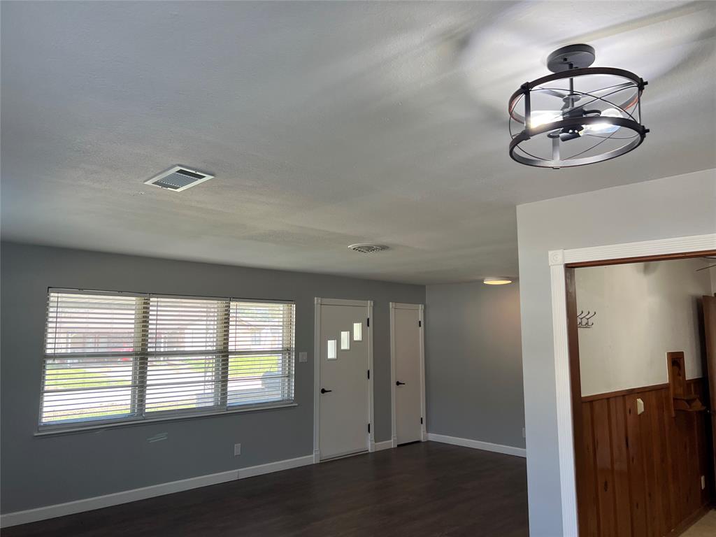 This room features modern lighting, large windows with blinds, and sleek dark flooring. The walls are painted in a neutral gray, offering a clean and open space.