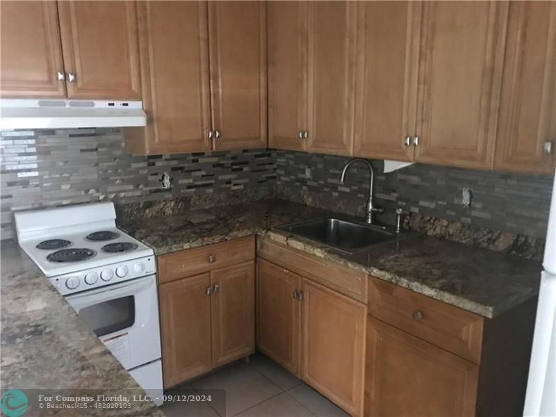 a kitchen with granite countertop a sink a stove and cabinets