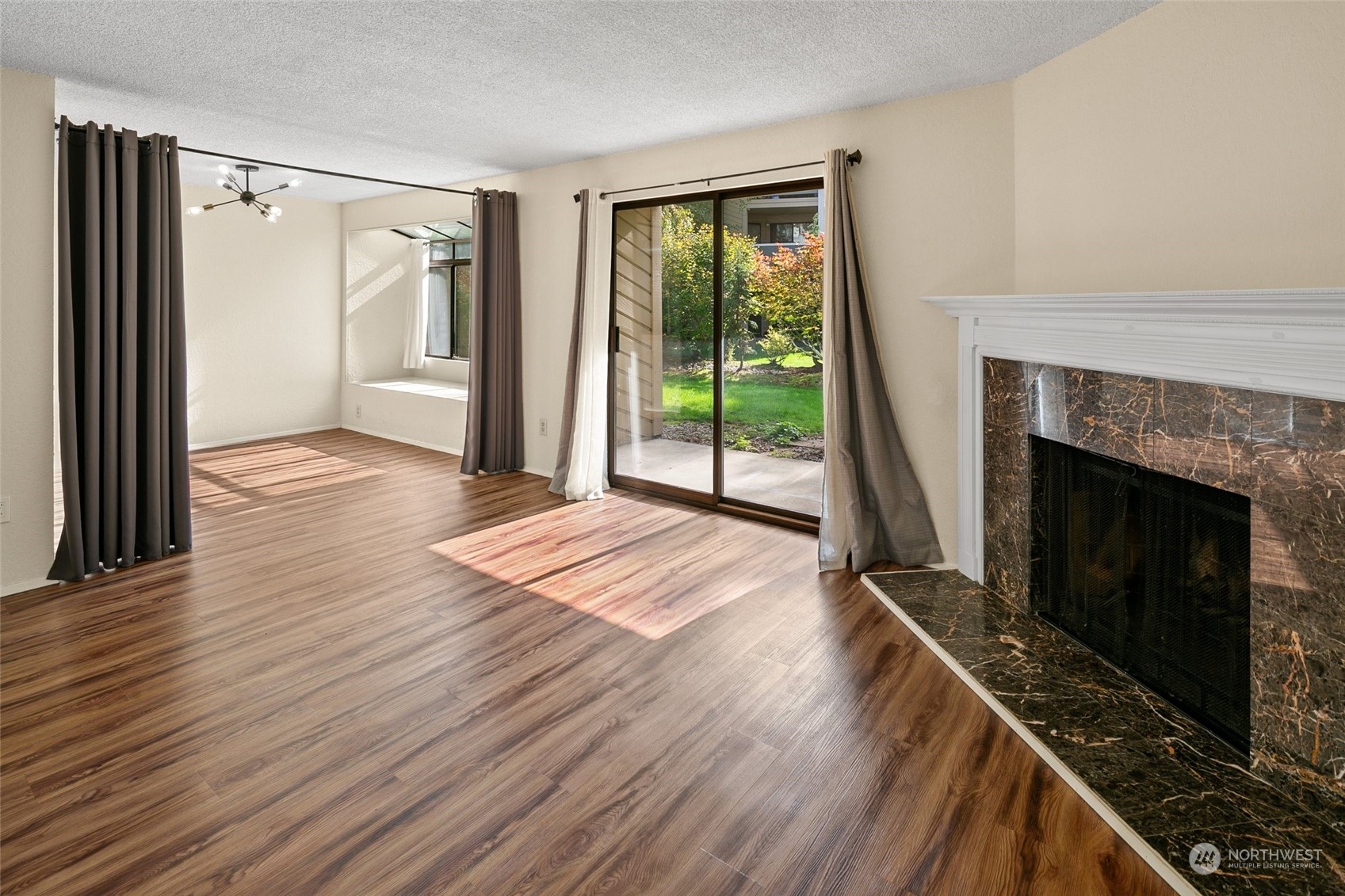 a view of an empty room with wooden floor fireplace and a window