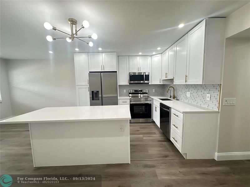 a large kitchen with stainless steel appliances a stove a sink dishwasher a refrigerator white cabinets and wooden floor