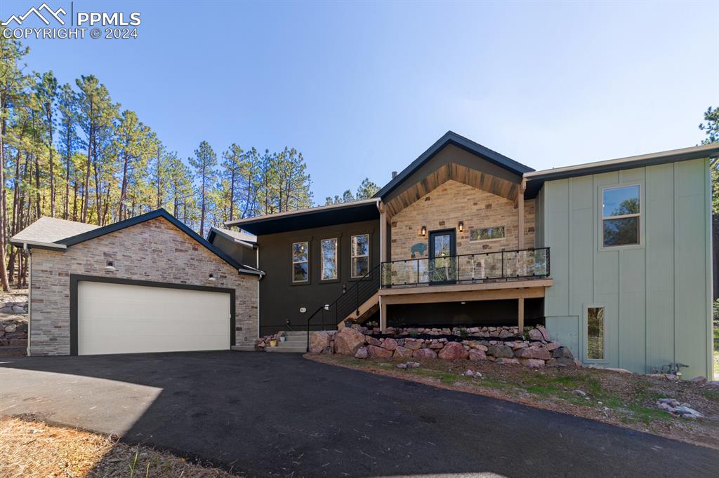 Front of home with oversized double garage and side-loaded third garage. Nestled among tall pines and open areas make for a very private place to call home.