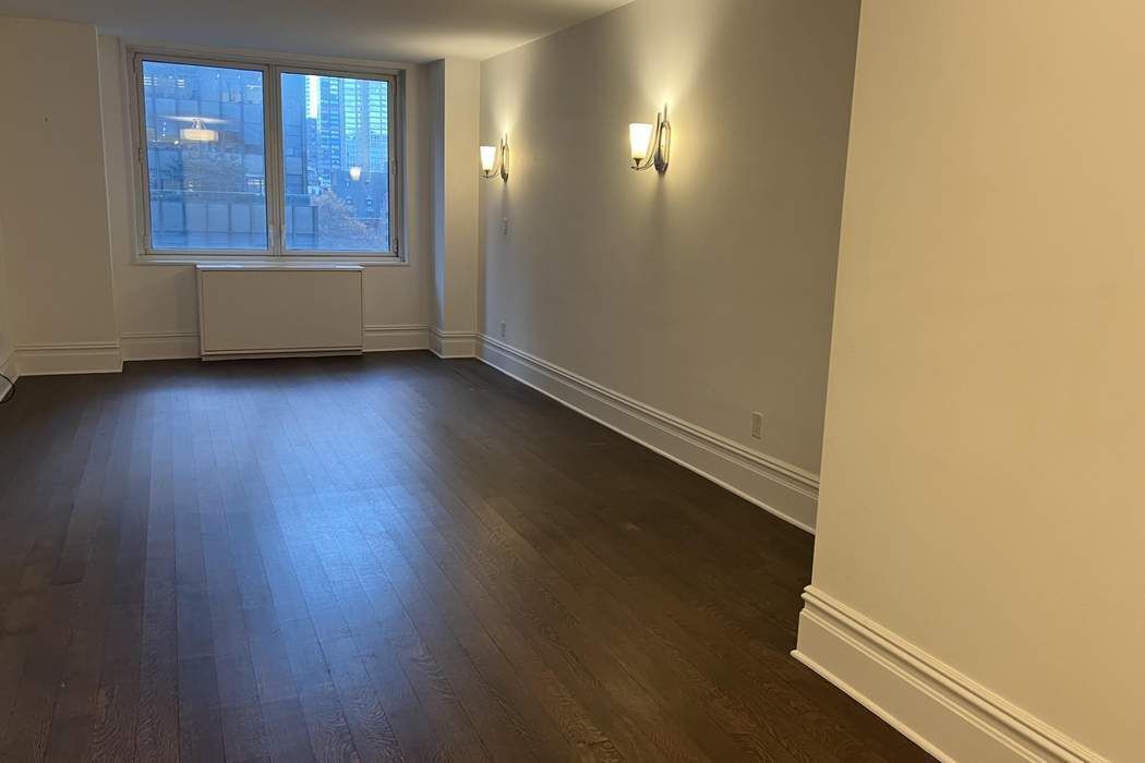 an empty room with wooden floor and windows with curtains