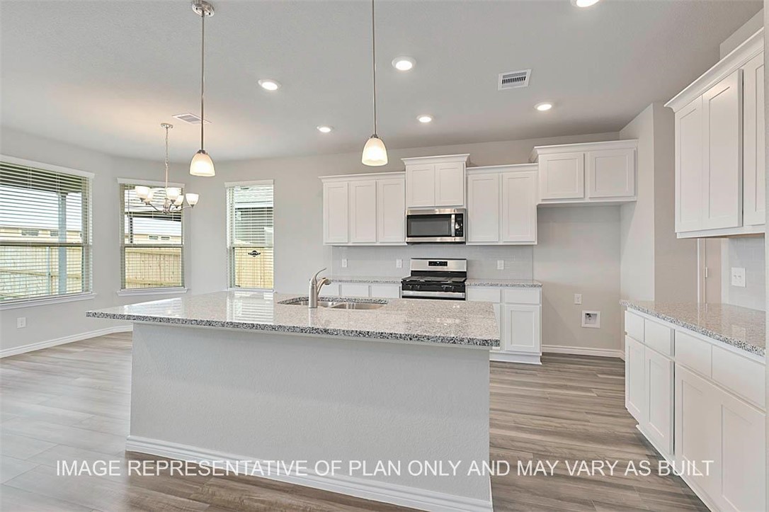 a kitchen with stainless steel appliances granite countertop a sink a stove a refrigerator and white cabinets