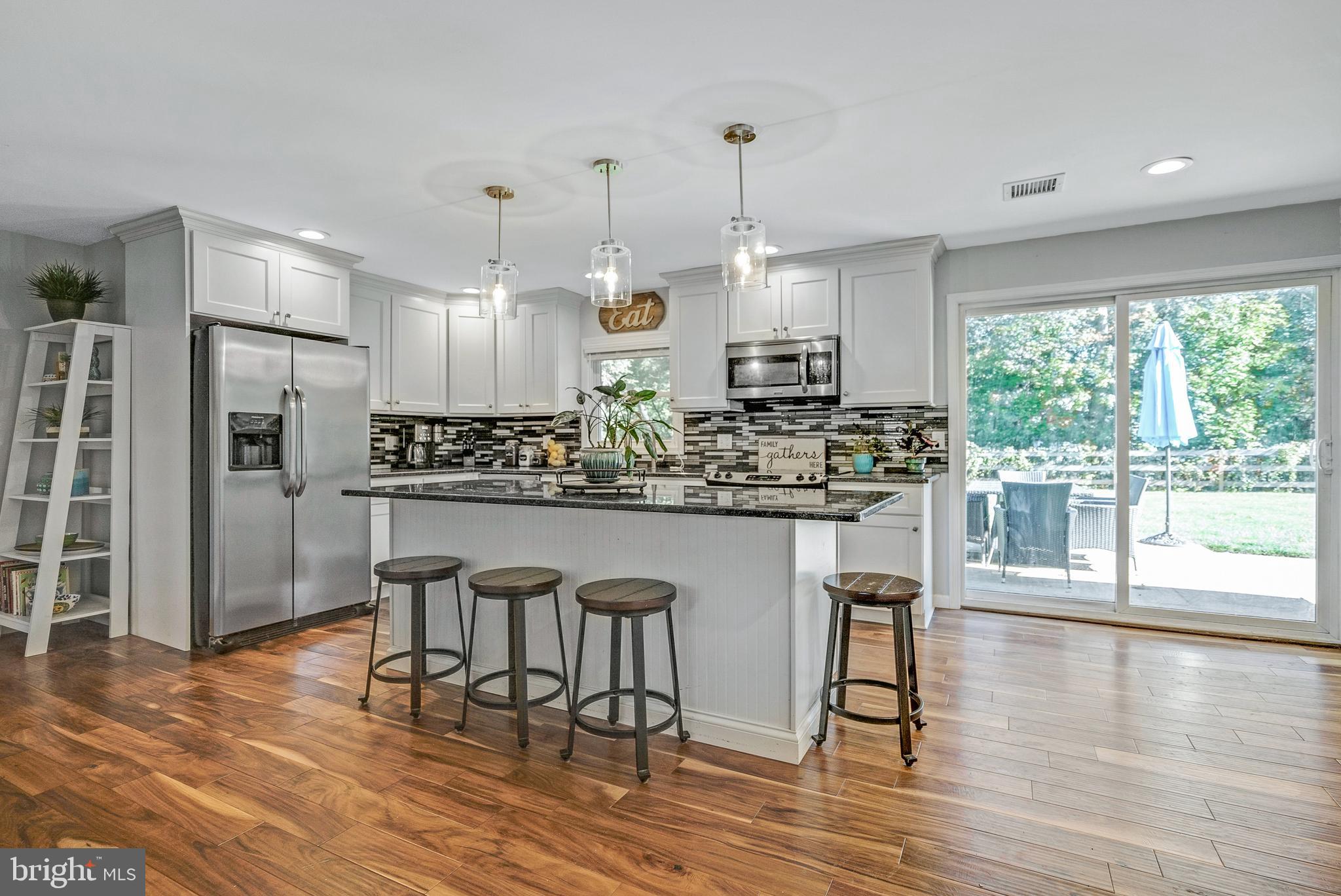 a kitchen with stainless steel appliances granite countertop a stove a refrigerator a kitchen island a dining table and chairs with wooden floor