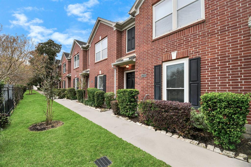 a brick house with a yard plants and big trees